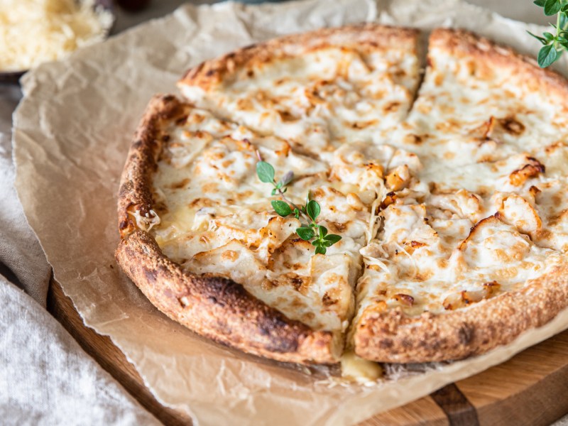 Pizza mit heller Soße auf Backpapier.