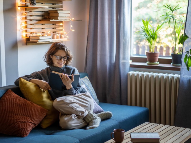 Frau sitzt auf Sofa und liest ein Buch.