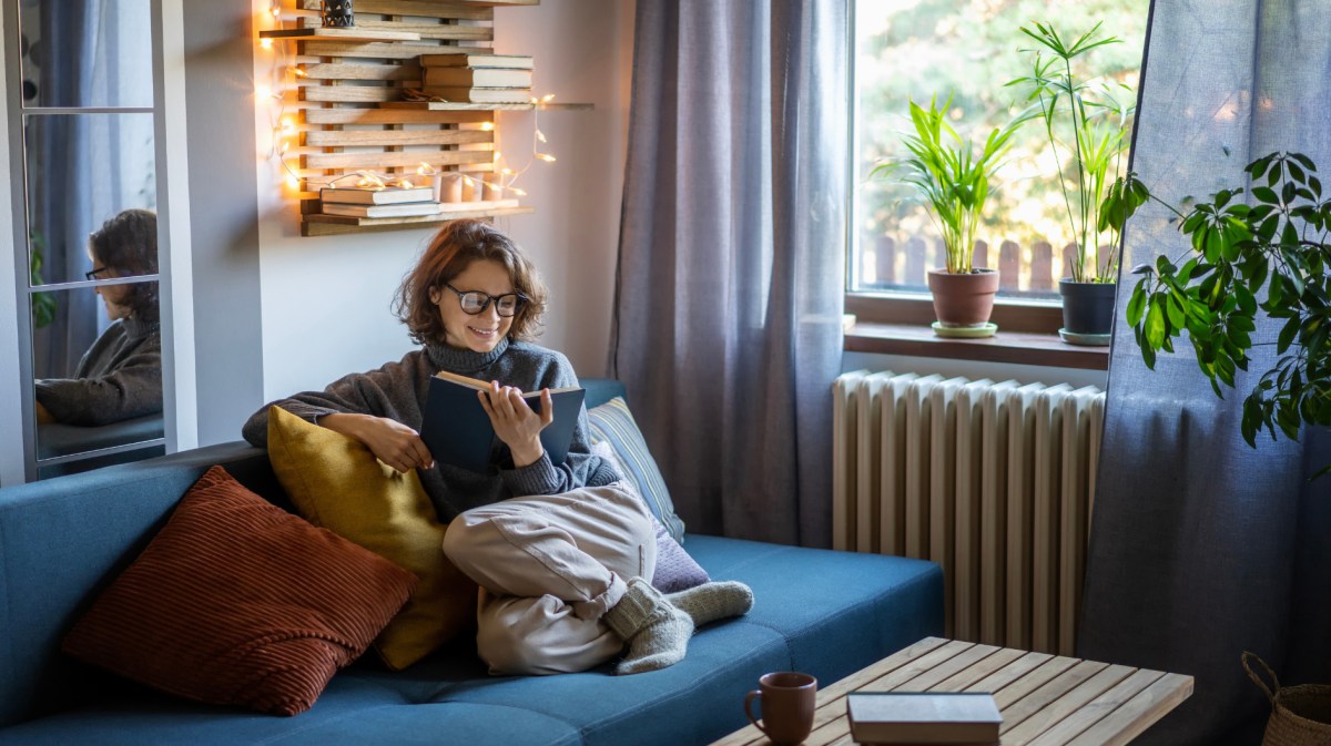 Frau sitzt auf Sofa und liest ein Buch.