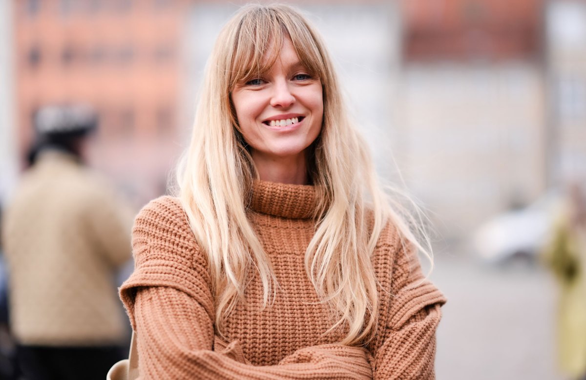 Blonde Frau mit hellbraunem Pullover lächelt in die Kamera.