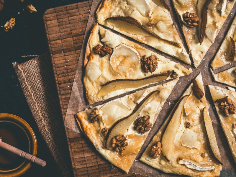 Flammkuchen mit Birne, Honig, Ziegenkäse und Walnüssen auf Holzuntergrund.