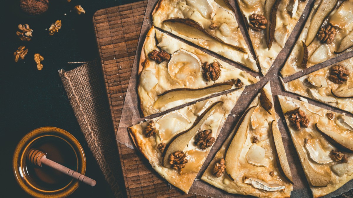 Flammkuchen mit Birne, Honig, Ziegenkäse und Walnüssen auf Holzuntergrund.