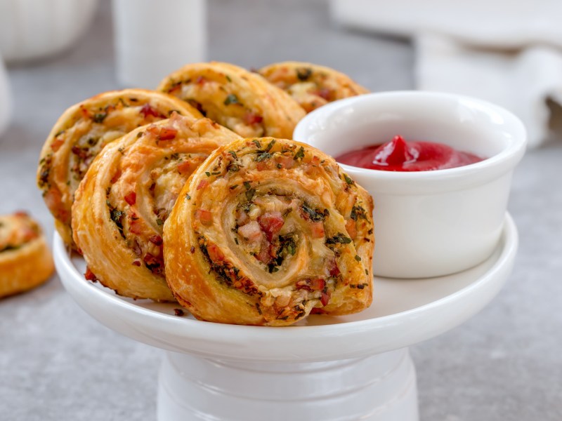 Blätterteig Schnecken mit Speckwürfel auf einem weißen Teller.