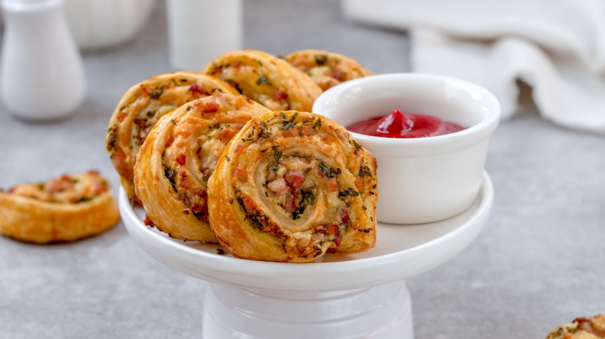 Blätterteig Schnecken mit Speckwürfel auf einem weißen Teller.