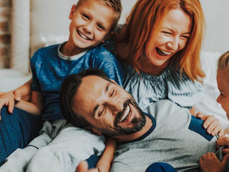 Mutter, Vater und zwei Kinder albern glücklich auf dem Sofa herum.