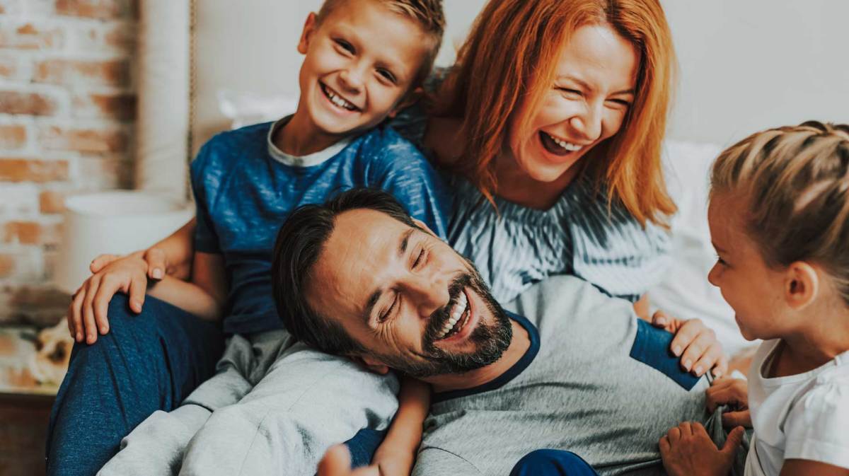 Mutter, Vater und zwei Kinder albern glücklich auf dem Sofa herum.