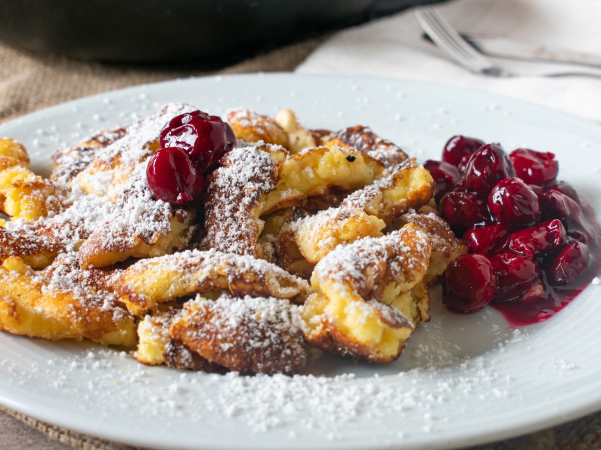 Kaiserschmarrn mit heißen Kirschen auf einem weißen Teller.