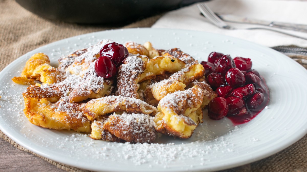 Kaiserschmarrn mit heißen Kirschen auf einem weißen Teller.