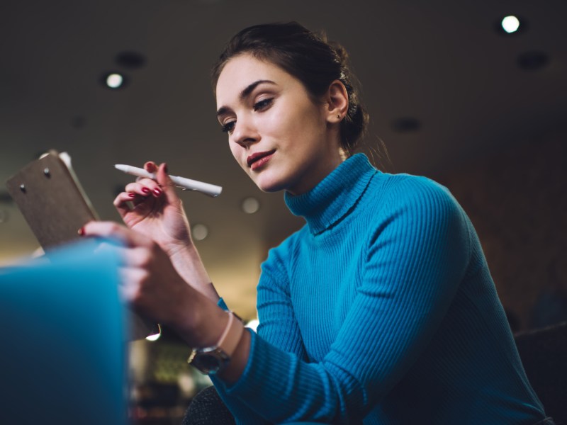 Frau in blauem Pullover schaut nachdenklich auf ihr Tablet.