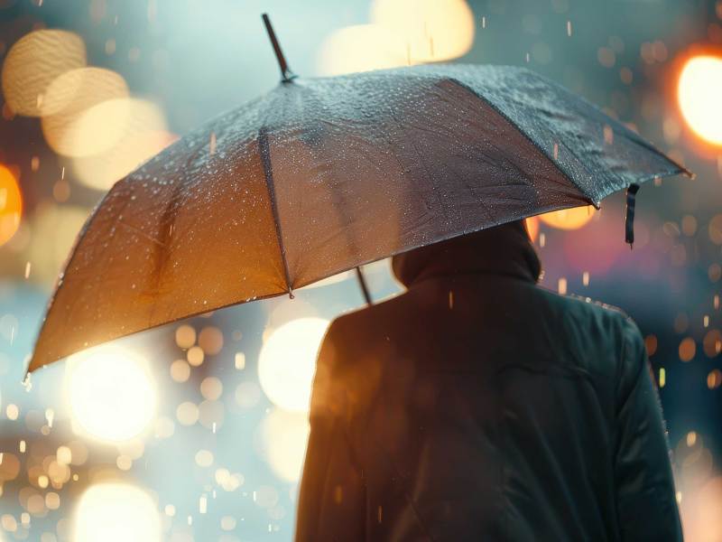 Eine Rückansicht einer Person, die einen Regenschirm hält, während sie inmitten eines regnerischen Abends in der Stadt steht