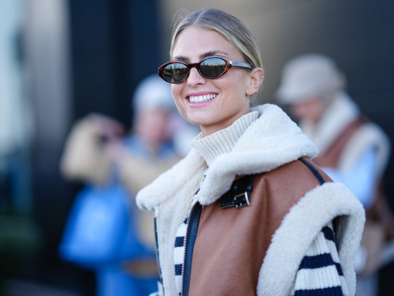 Frau mit Sonnenbrille lächelt und trägt Fellweste