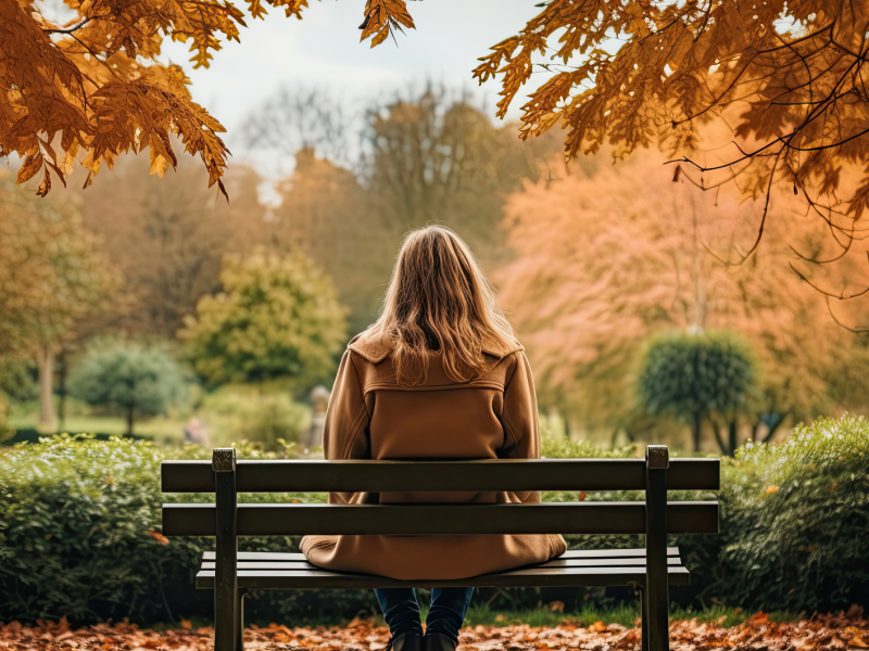 Eine Frau alleine auf einer Parkbank im Herbst.