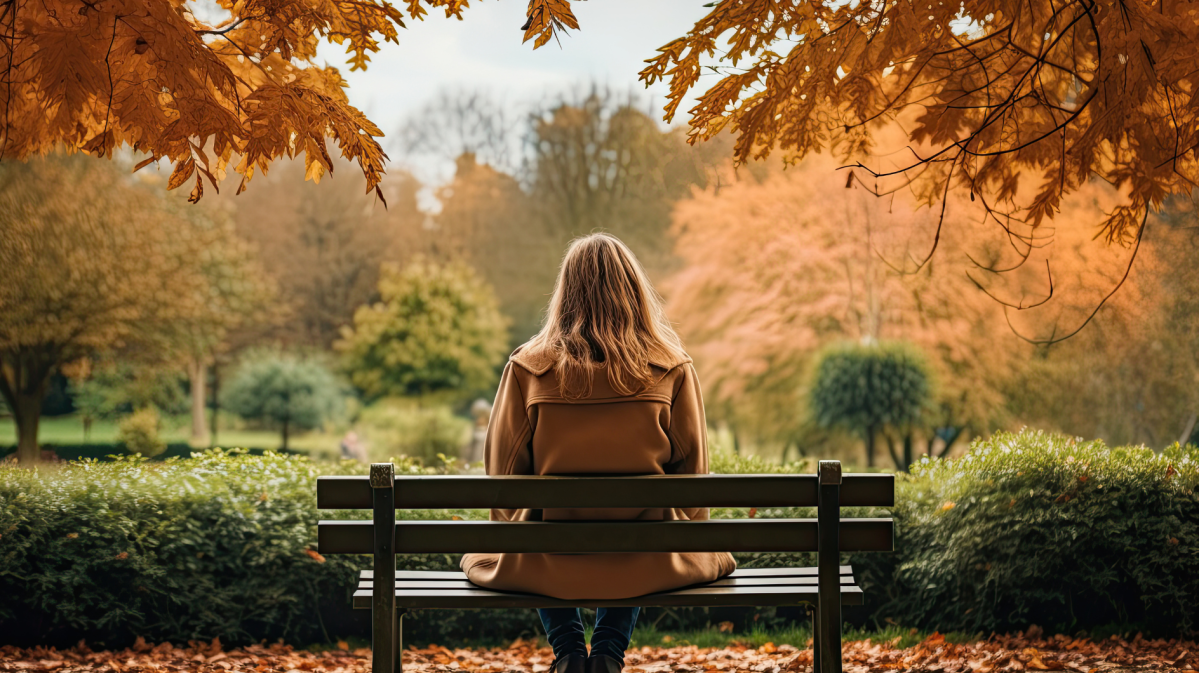 Eine Frau alleine auf einer Parkbank im Herbst.