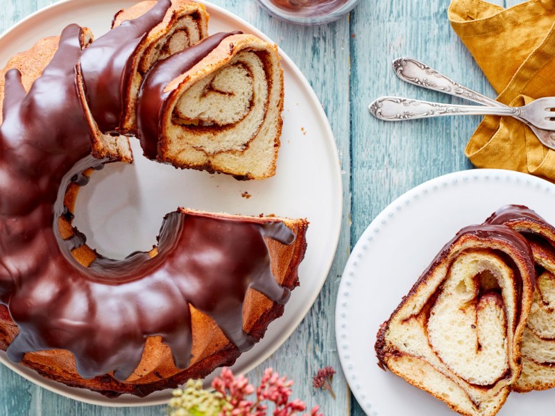 Zimtschnecken-Gugelhupf auf einem weißen Teller auf hellblauem Holztisch.