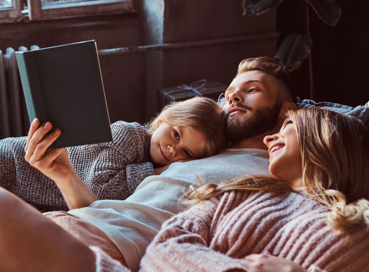 Familie liegt auf dem Bett beim Vorlesen aus einem Buch