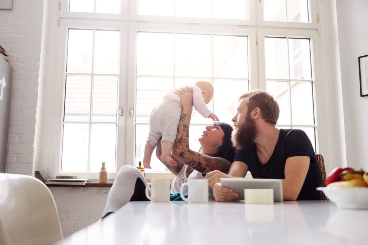 Vater und Mutter sitzen am Tisch und heben ihr Baby in die Luft