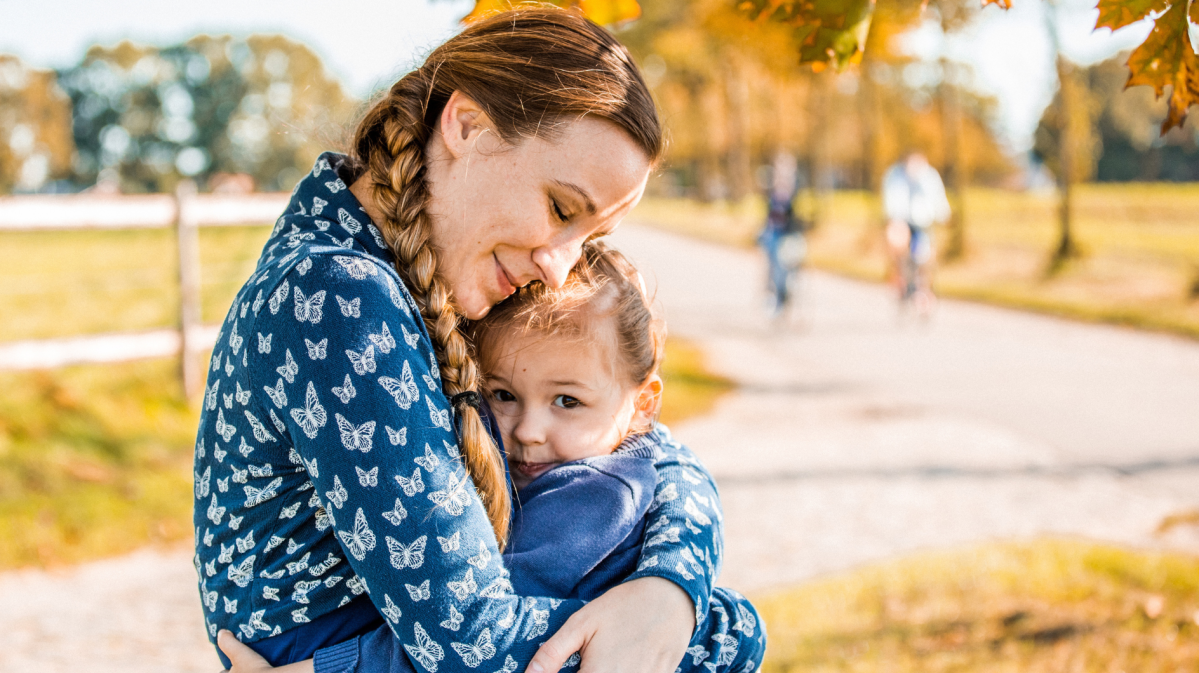 Mutter und Kind sitzen im Park auf einer Bank und umarmen sich