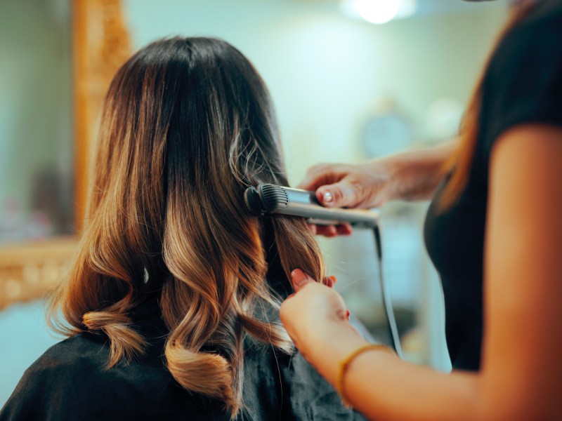 Frau bekommt Locken mit dem Glätteisen gemacht