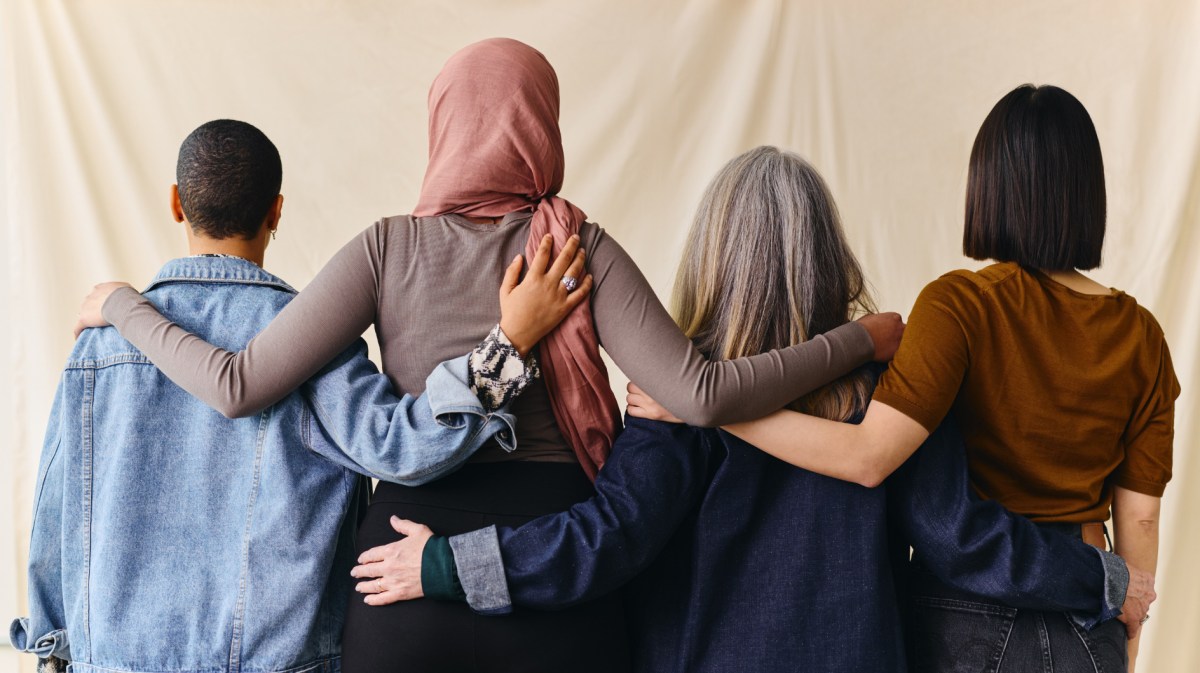 Vier Frauen stehen mit Rücken zur Kamera, haben ihre Arme um die Schultern gelegt.