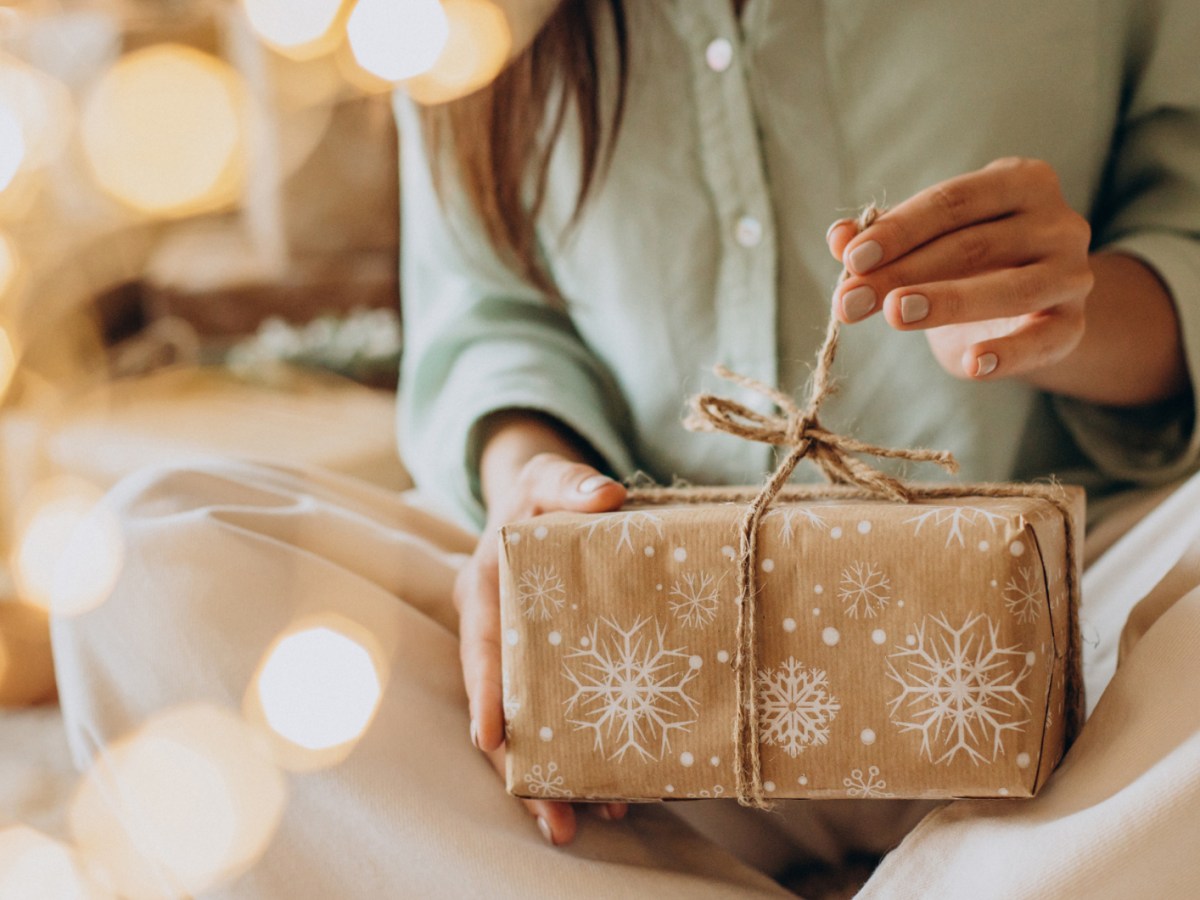 Frau öffnet Weihnachtsgeschenk, das sie im Schoß hält.