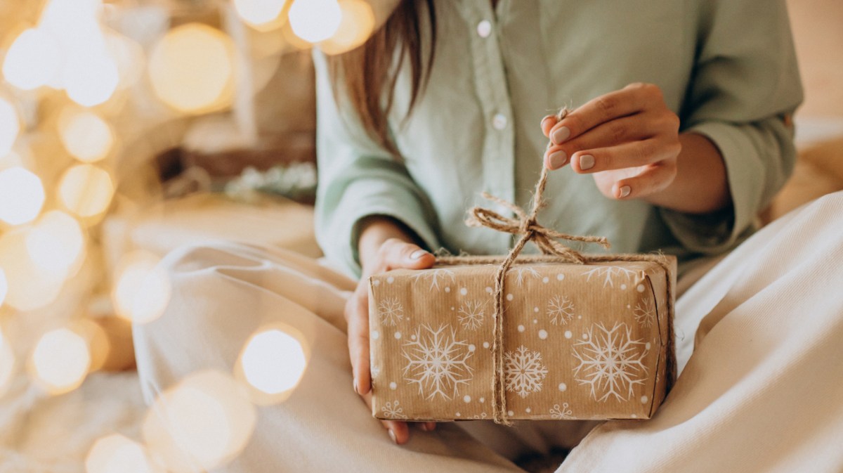 Frau öffnet Weihnachtsgeschenk, das sie im Schoß hält.