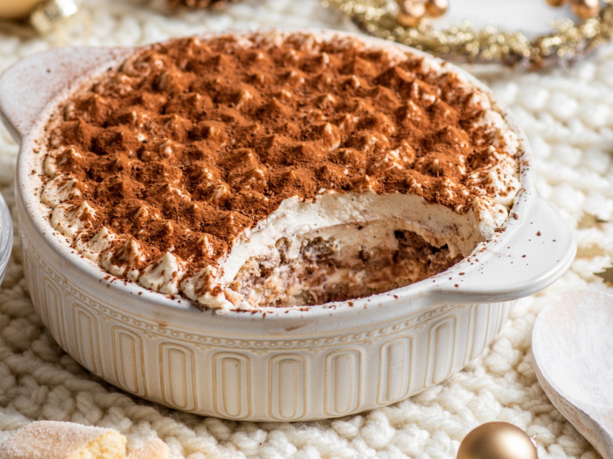 Tiramisu in weißer Auflaufform auf weihnachtlich gedecktem Tisch.