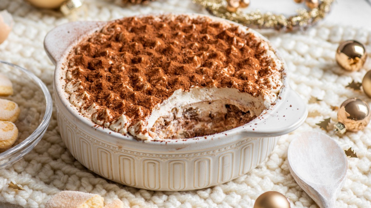 Tiramisu in weißer Auflaufform auf weihnachtlich gedecktem Tisch.