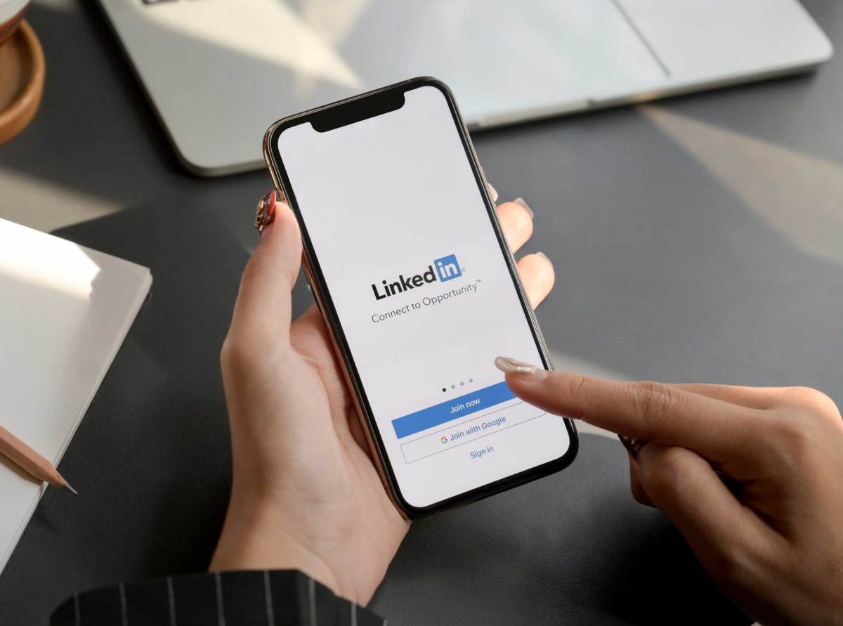 Frau berührt iPhone mit LinkedIn-Bildschirm. LinkedIn hilft beim Erstellen des Lebenslaufs und bei der Suche nach einem neuen Job