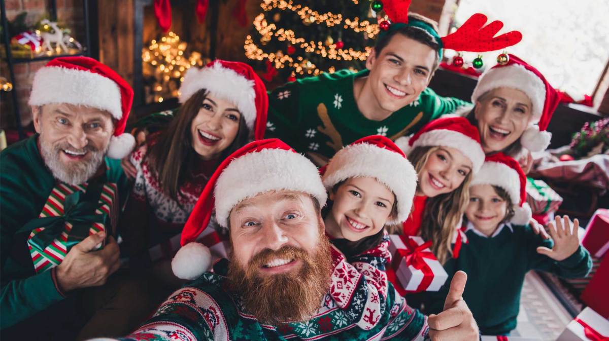 Selfie einer Familie, bestehend aus 8 Personen, die alle Weihnachtspulli und -mütze tragen und vor einem Weihnachtsbaum posieren.