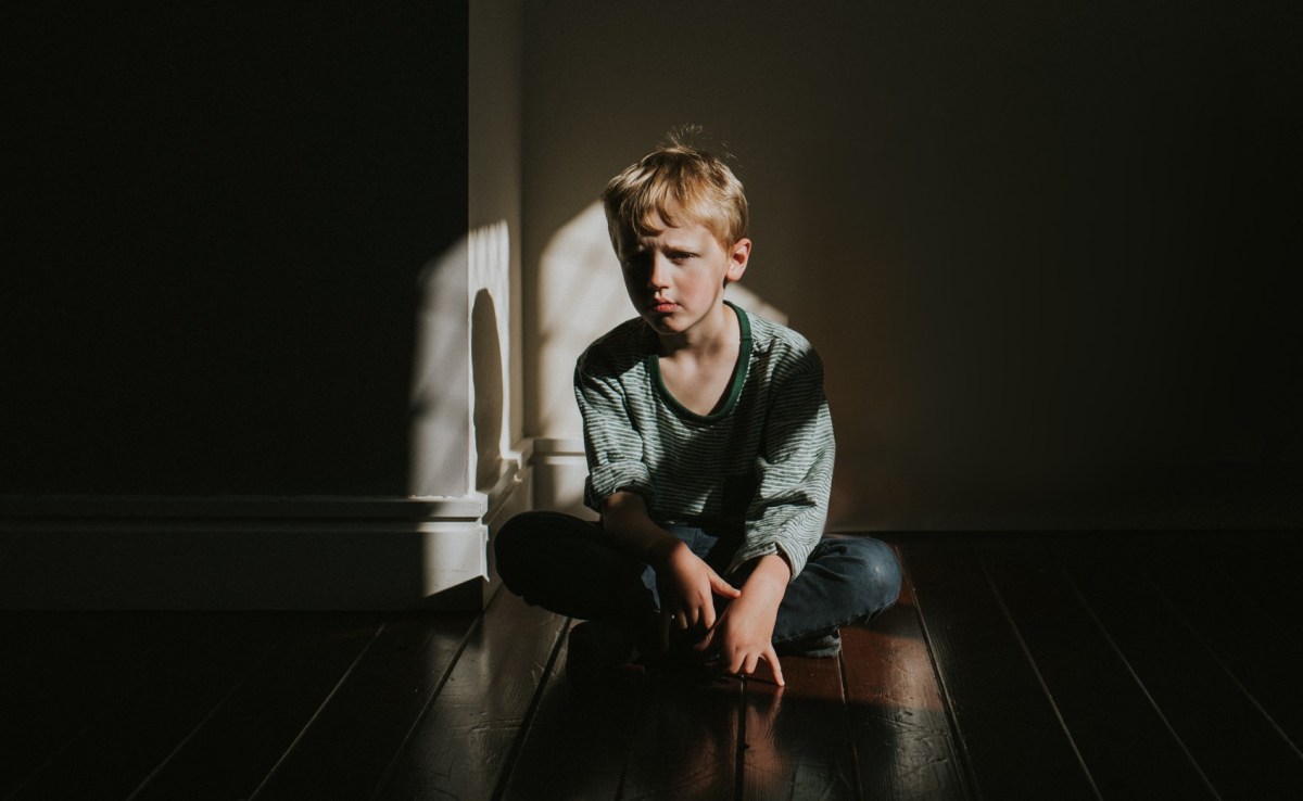 Junge sitzt im Schatten auf dem Boden und wirkt traurig