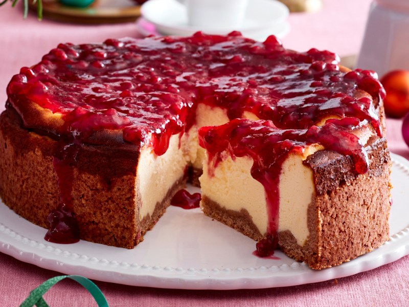 Käsekuchen mit Preiselbeer-Topping auf einem weißen Teller.