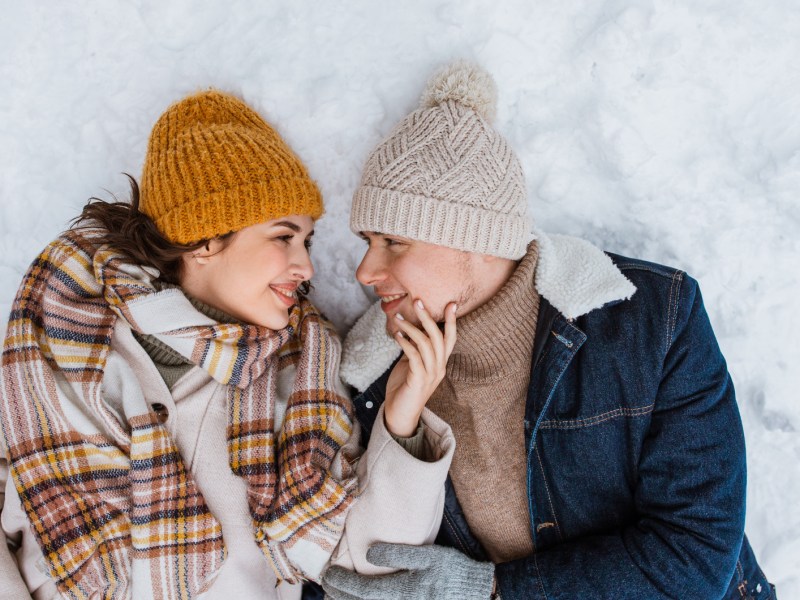 Pärchen liegt im Schnee und schaut sich verliebt an.