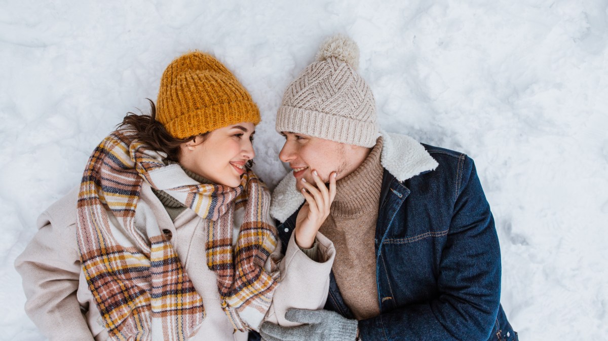 Pärchen liegt im Schnee und schaut sich verliebt an.