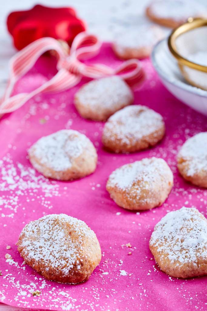 Mini-Stollen-Kekse auf einem pinken Untergrund, mit Puderzucker bestäubt.