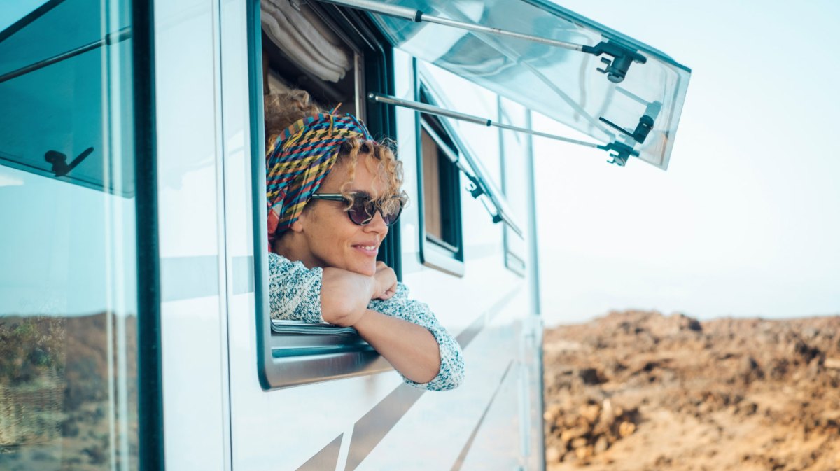 Frau mit Sonnenbrille schaut aus offenem Fenster eines Wohnmobils