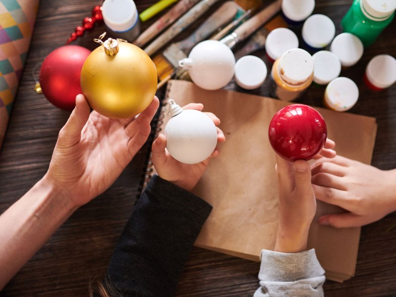 Nahaufnahme von Kinderhänden, die im Bastelkurs Weihnachtskugeln über einem Holztisch halten