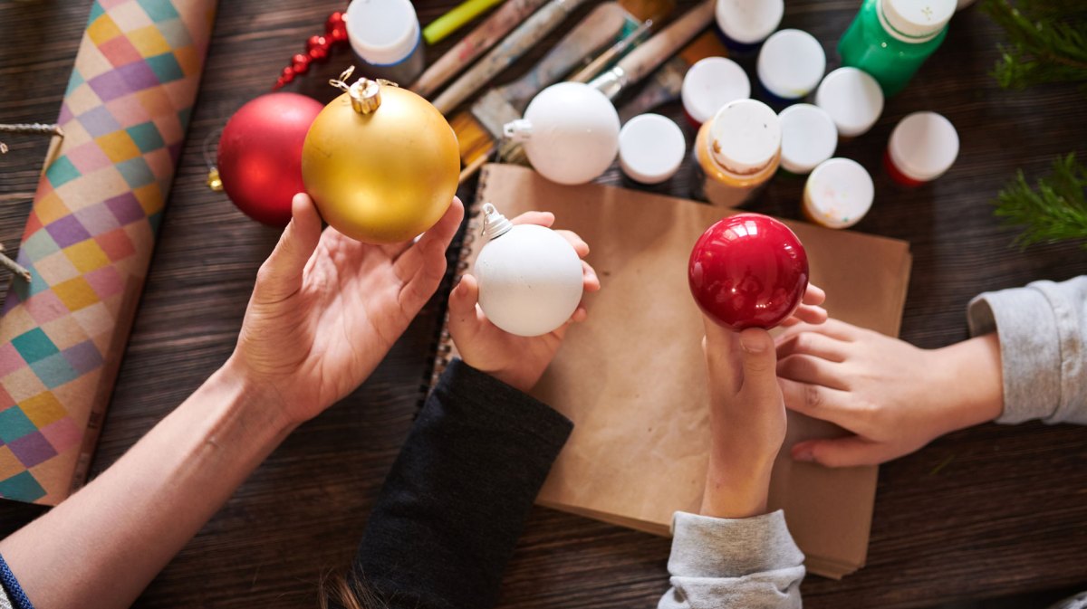 Nahaufnahme von Kinderhänden, die im Bastelkurs Weihnachtskugeln über einem Holztisch halten