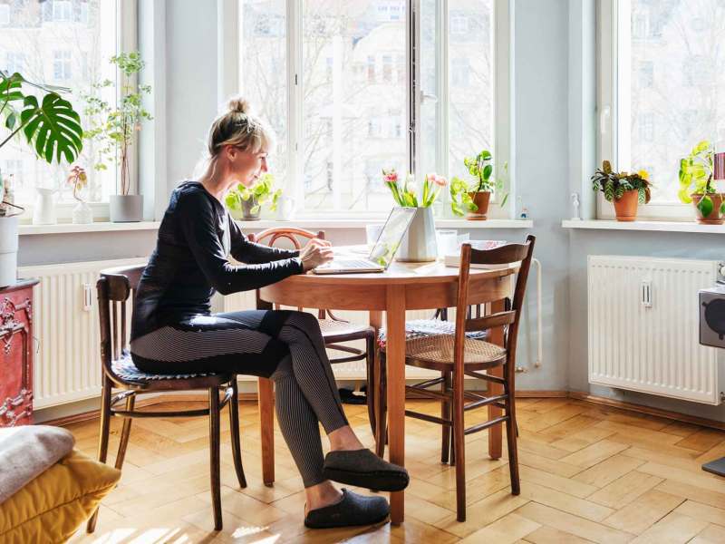 Frau sitzt in beqeuemer Kleidung zu Hause im Homeoffice am Küschentisch.