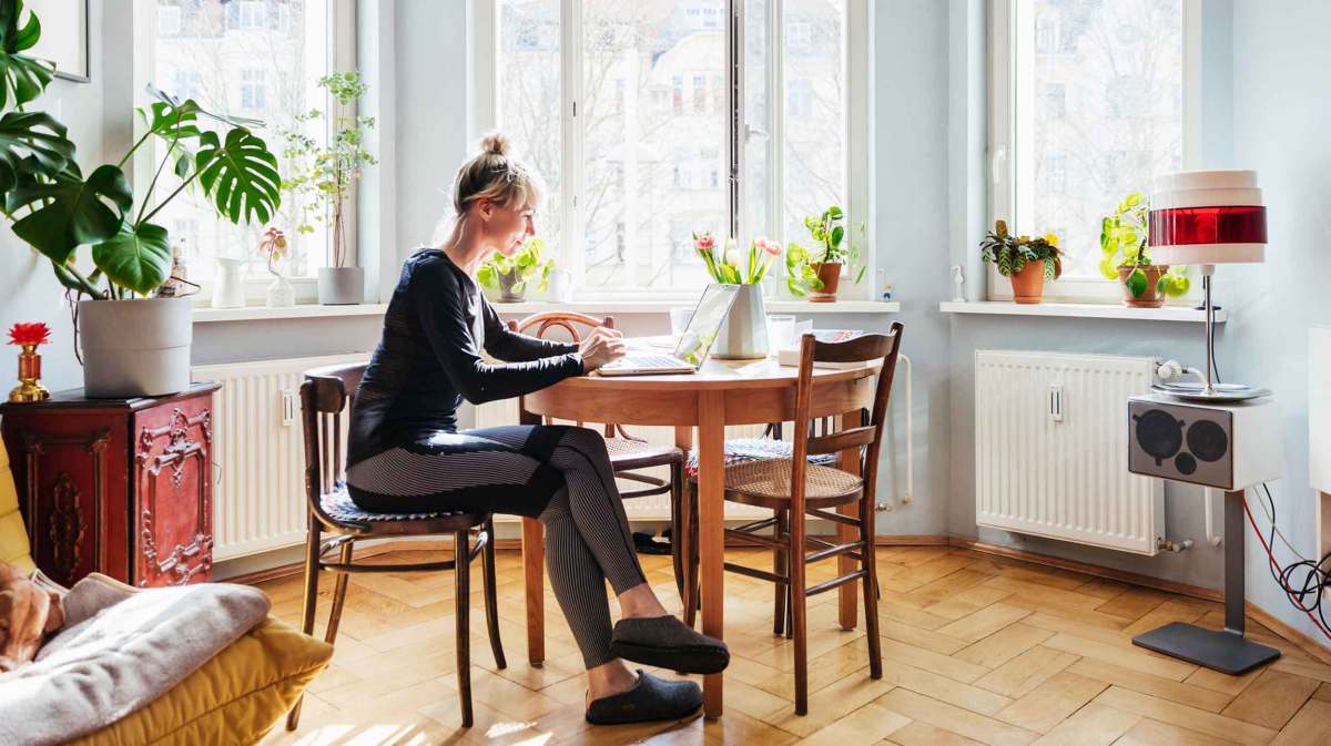 Frau sitzt in beqeuemer Kleidung zu Hause im Homeoffice am Küschentisch.