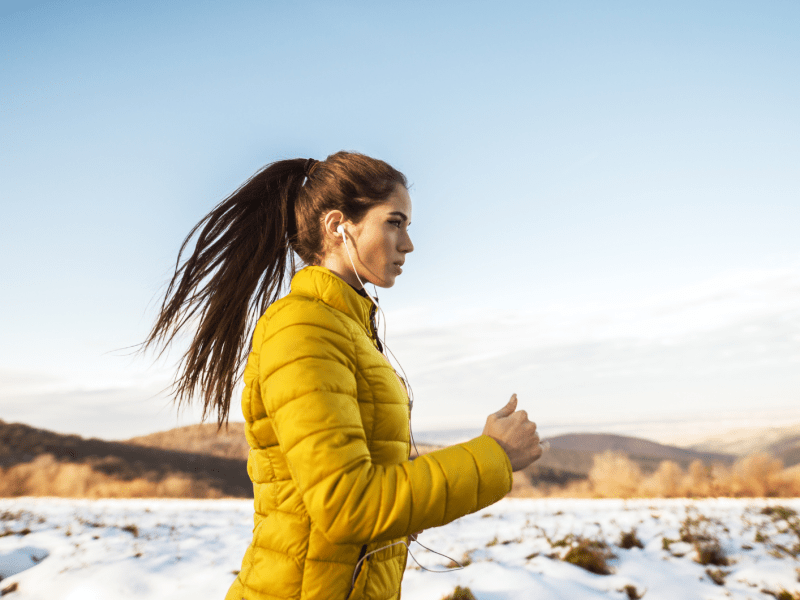 Frau in Winterlandschaft mit gelber Jacke, die am Laufen ist.