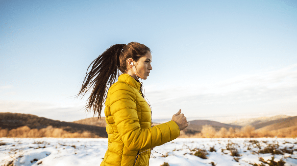 Frau in Winterlandschaft mit gelber Jacke, die am Laufen ist.