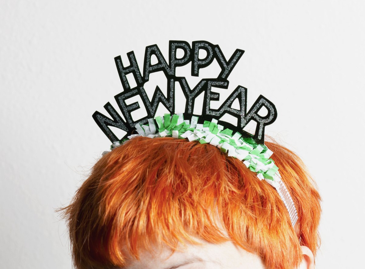 Frau mit orangen Haaren und Happy New Year Haarreif auf dem Kopf.