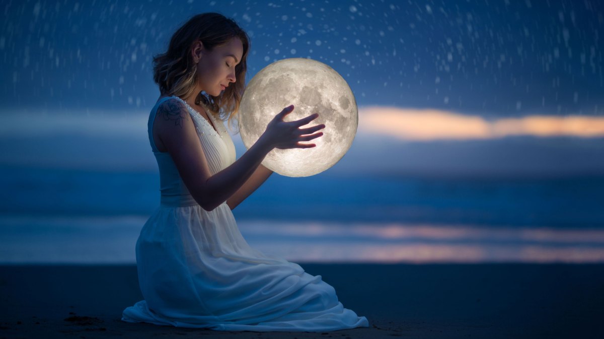 Frau im weißen Kleid bei Dämmerung am Strand hält Mond in der Hand