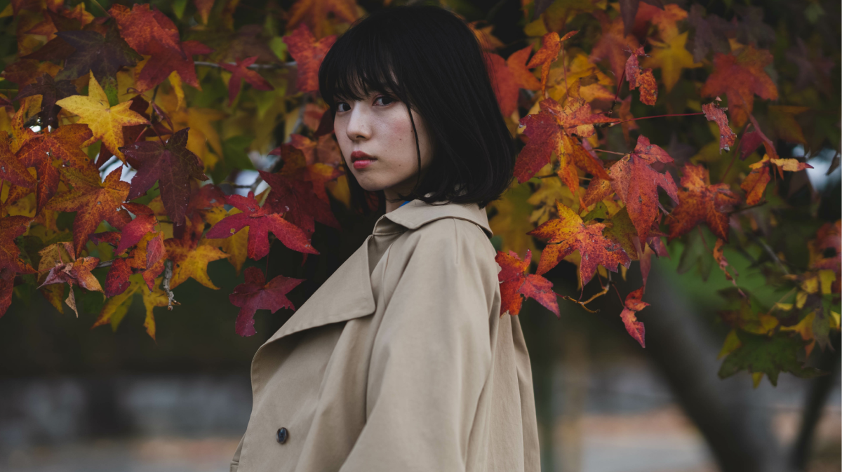 Asiatische Frau vor herbstlichen Blättern, die sich mit düsterem Blick umdreht.