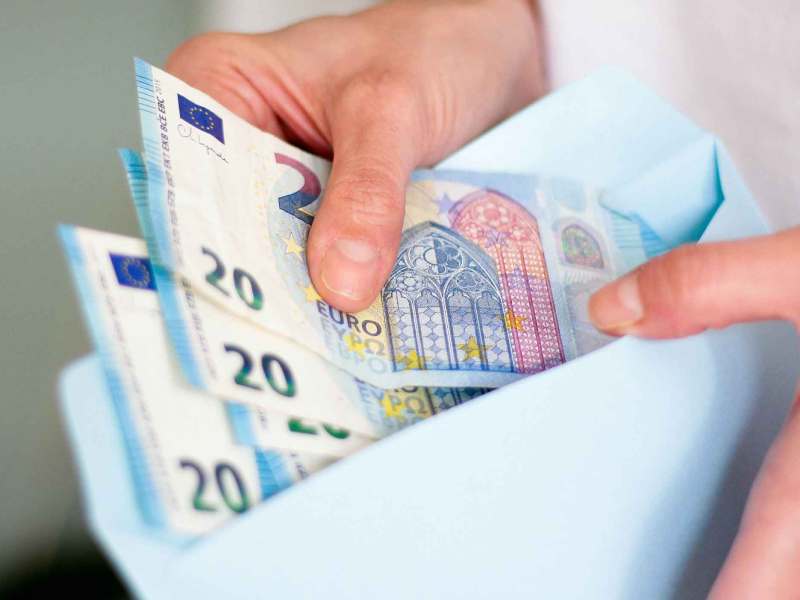 Frau schiebt drei 20-Euro-Scheine in einen Umschlag.