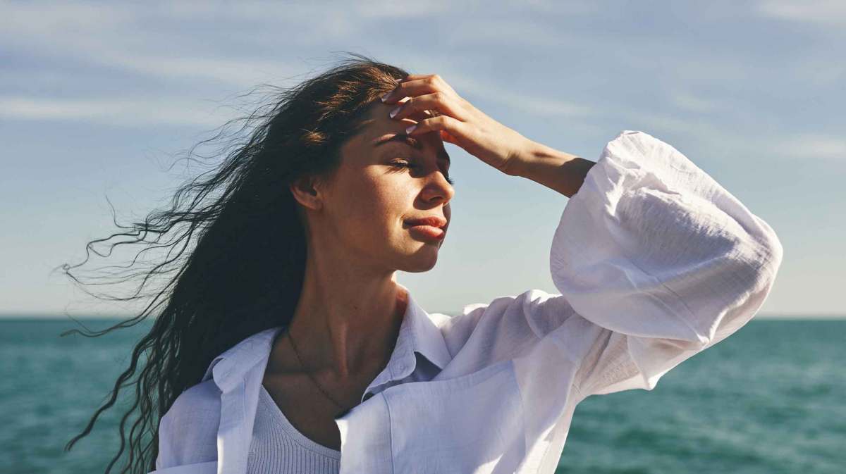 Junge Frau mit langen dunklen Haaren steht am Meer.