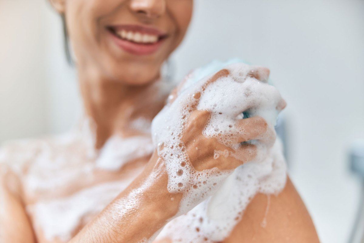 Frau, die unter der Dusche steht und sich mit viel Schaum einseift.