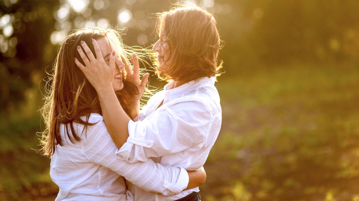 Mutter und Tochter im Teenageralter umarmen sich draußen, umgeben von weichem Sonnenlicht.