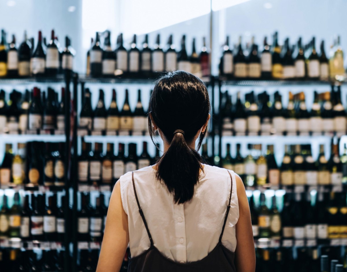 Frau steht vor einem Regal mit Weinflaschen im Supermarkt.