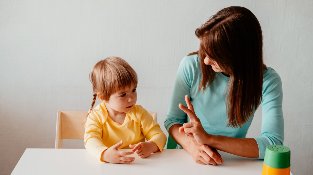 Mutter sitzt mit ihrem Kleinkind am Tisch und bringt ihm Zahlen bei